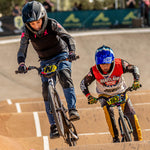 Two BMX riders in full gear race on a dirt track, one lifting the front wheel, at the National Championships—captured by the LUXBMX Race Photo Package.