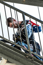 Captured during the National Championships, a man in motocross gear stands behind a metal staircase holding his helmet—partially obscured by railings. Photo from the LUXBMX Race Photo Package.