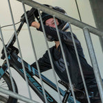 Dressed in black biking gear and helmet, a rider pushes a "SPEED" bicycle up a ramp behind a metal railing, captured in the LUXBMX Race Photo Package ahead of the National Championships.