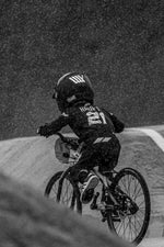 A cyclist in helmet and jersey rides a bike on a wet track in the rain during the National Championships, captured from behind for the LUXBMX Race Photo Package.