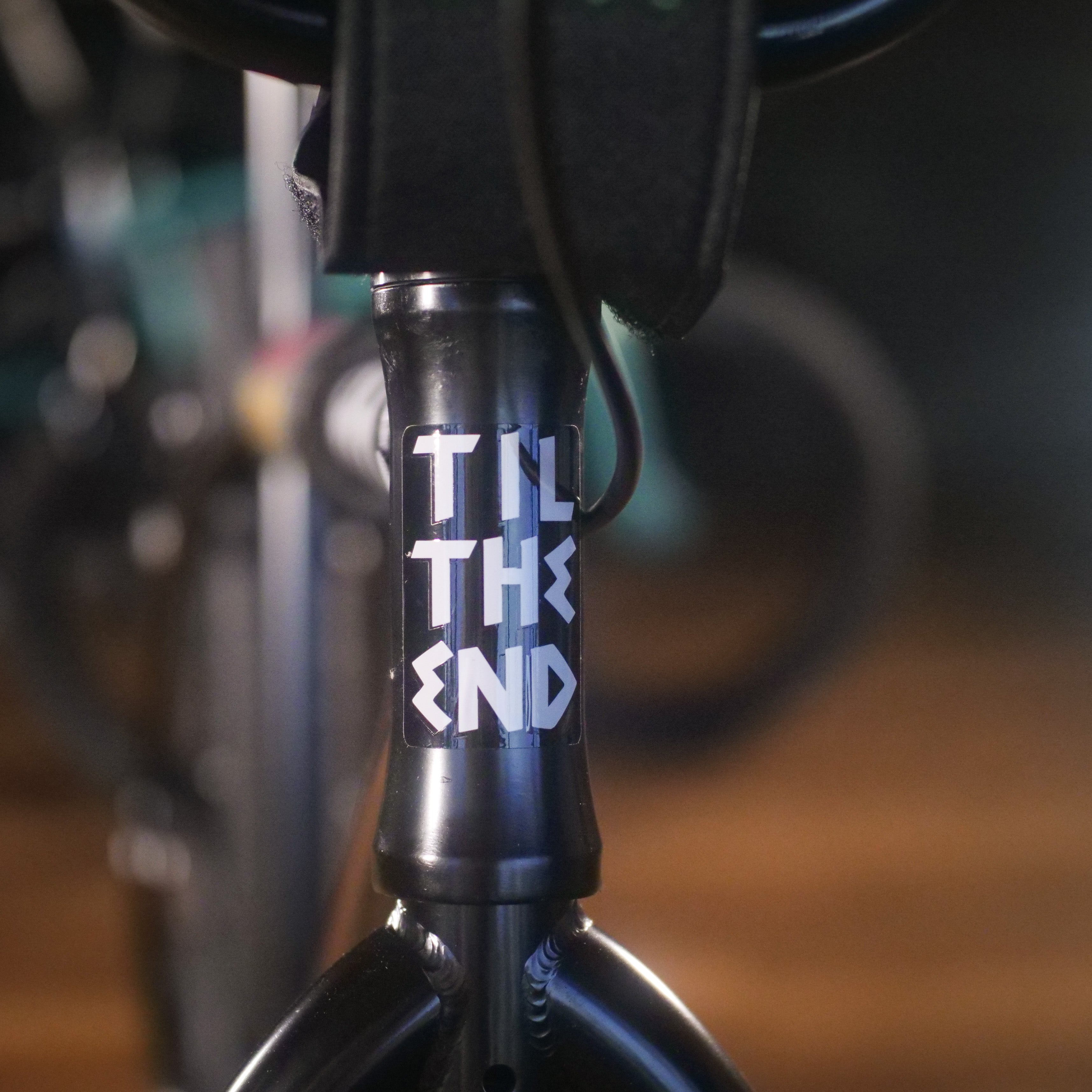 Close-up of the Cult Devotion 26 Inch Bike's head tube featuring "TIL THE END" in bold white letters, with the Chromoly frame standing out against a blurred background.