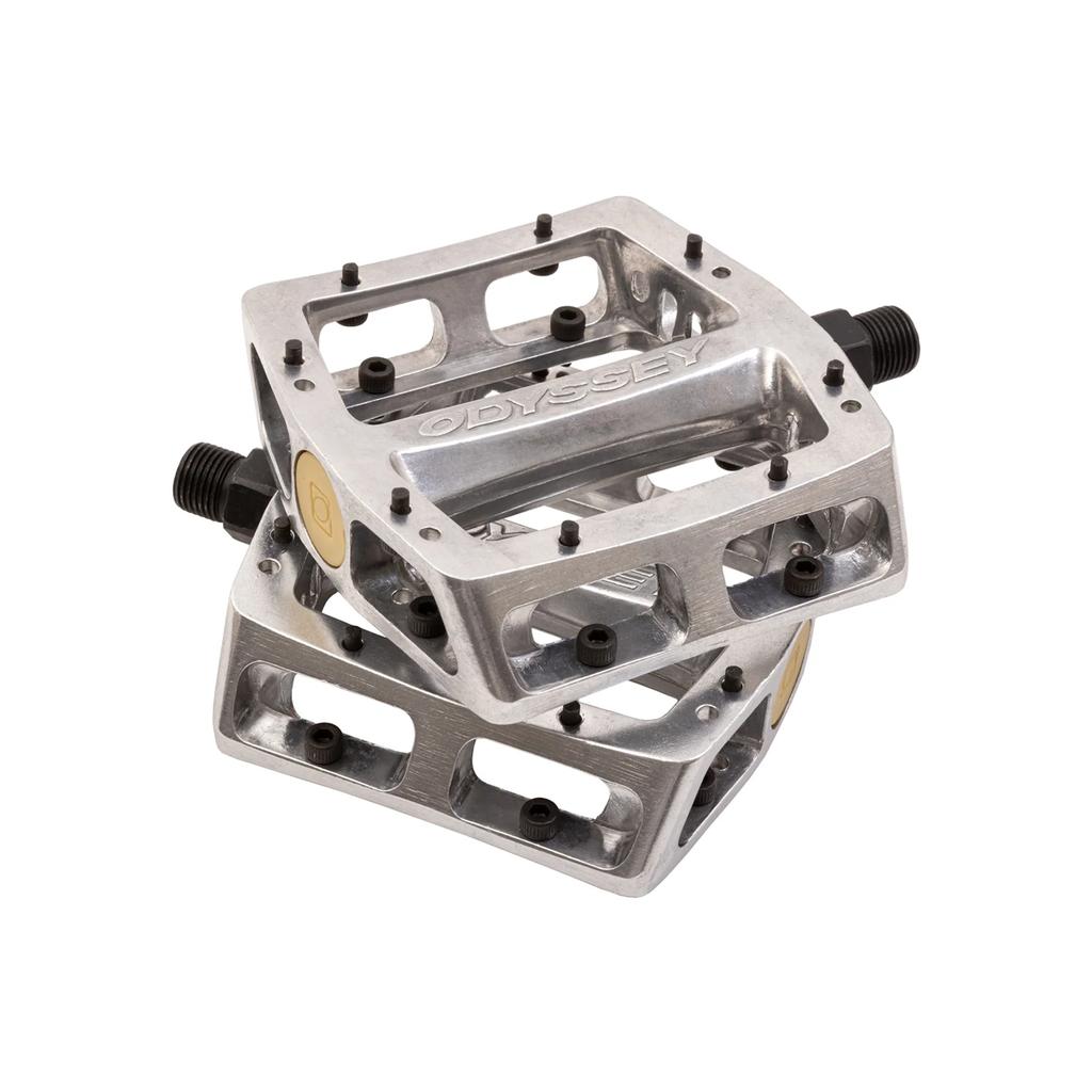 Two silver Odyssey Trail Mix Loose Ball Pedals, featuring aluminium bodies, black pins, hollow sections, and visible Odyssey branding, are stacked on top of each other.