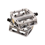 Two silver Odyssey Trail Mix Loose Ball Pedals, featuring aluminium bodies, black pins, hollow sections, and visible Odyssey branding, are stacked on top of each other.
