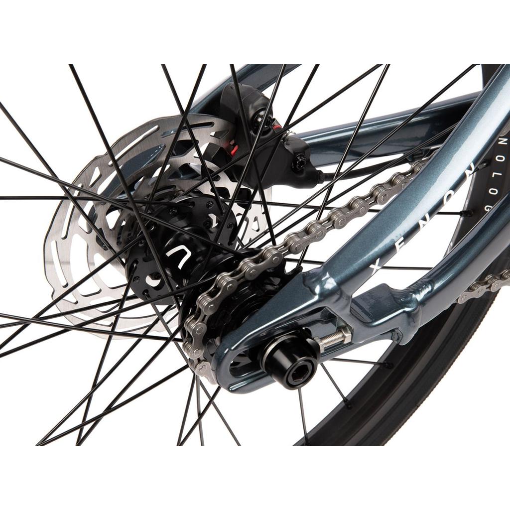Close-up of the Radio Xenon Expert XL Disc 20 Inch Bike's rear wheel, highlighting the chain, cassette, disc brake rotor, and spokes on its metallic blue lightweight alloy frame with pro-level components.