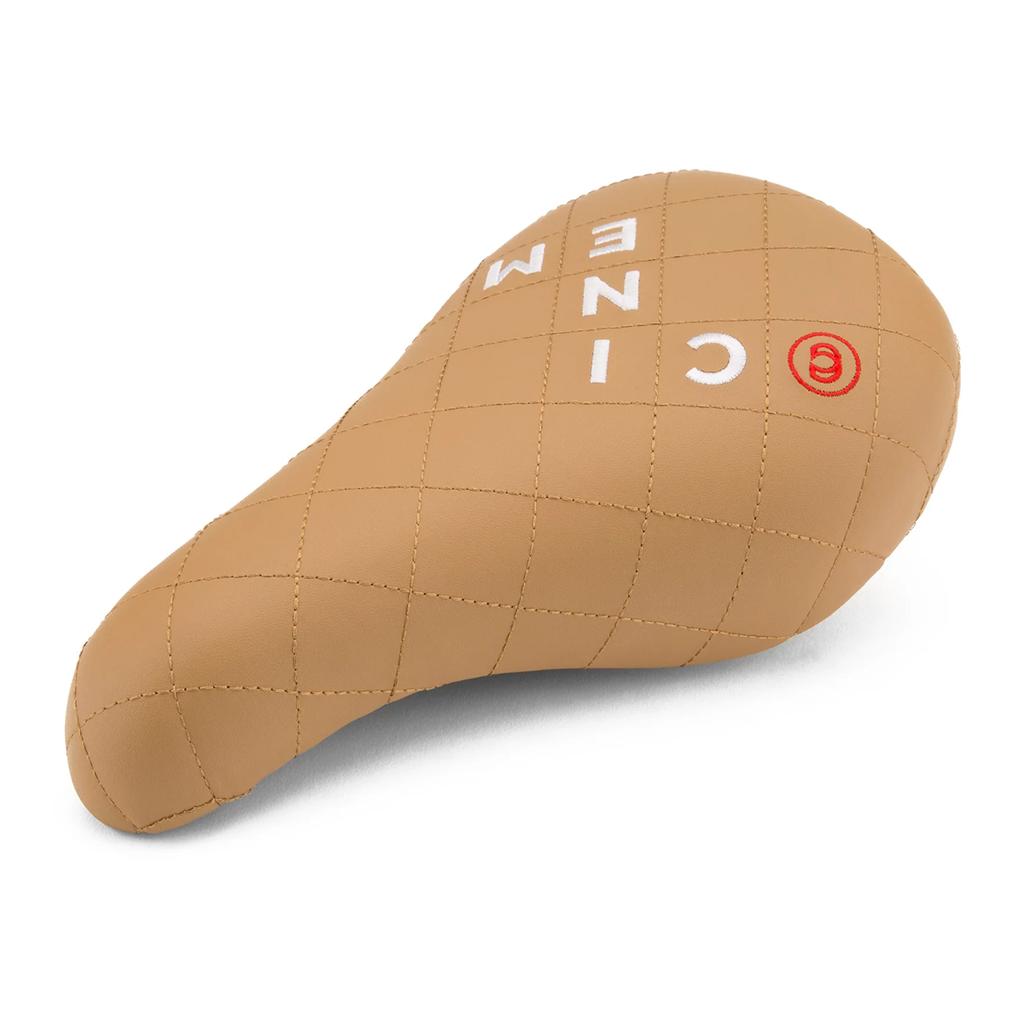 The Cinema Blocked Stealth Seat is a tan faux leather bicycle seat with a quilted pattern, white stitched "CINEMA" text, Stealth technology, and a red circle logo on the right side.
