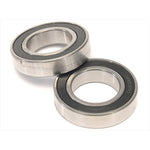 Two Eclat Pulse Hub Bearing Set (Rear) metal ball bearings with black rubber seals are on a white surface—one upright, one flat—designed for bicycle hub use.