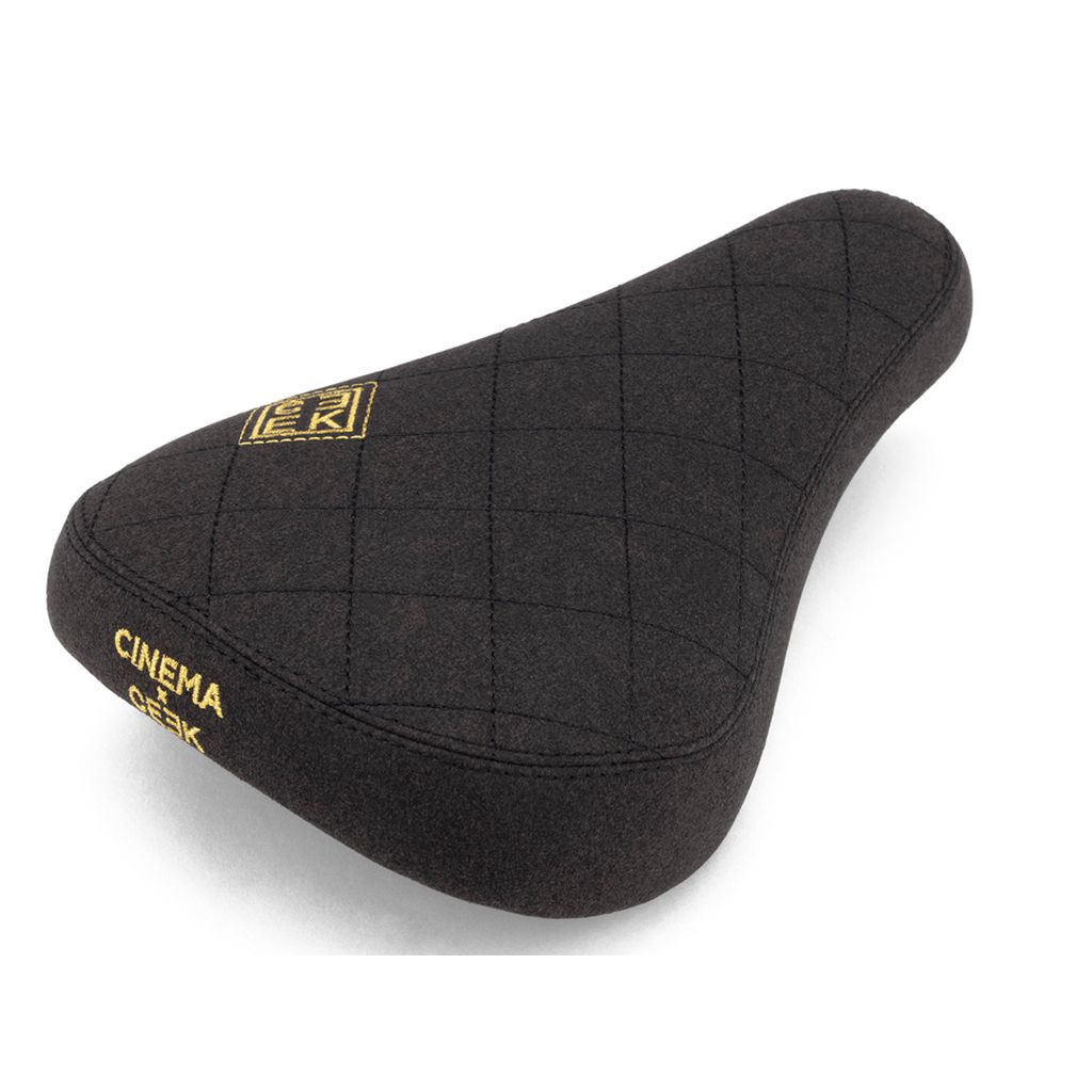 The Cinema CEEK 2 Stealth Pivotal Seat is a black bike seat with quilted stitching, yellow "Cinema" and "OGK" branding, and a durable microfiber cover.