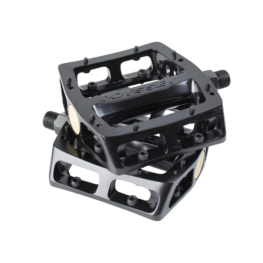 A pair of black Odyssey Trail Mix Loose Ball Pedals with aluminum bodies, open sides, and small traction pins are stacked together. "Odyssey" is embossed on the top pedal.