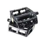 A pair of black Odyssey Trail Mix Loose Ball Pedals with aluminum bodies, open sides, and small traction pins are stacked together. "Odyssey" is embossed on the top pedal.