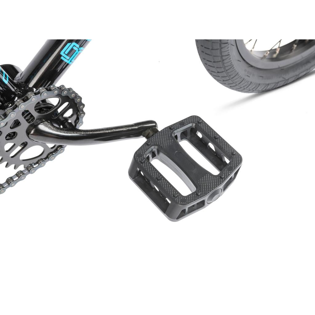 Close-up of a black pedal, crank arm, chainring, and rear wheel on a white Radio Revo 16 Inch Bike.