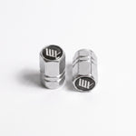 Two LUXBMX Hex Logo Alloy Valve Caps stand upright on a white surface, each resembling machined metal and featuring the LUX logo on top.