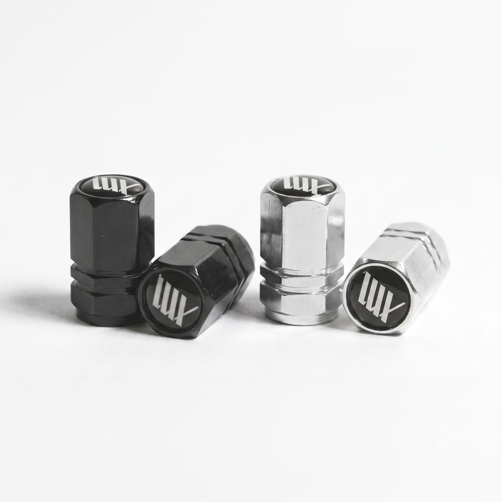 Two pairs of LUXBMX Hex Logo Alloy Valve Caps—one black, one silver—are displayed on a white surface, each showcasing the signature "LUX" logo found on premium LUXBMX accessories.
