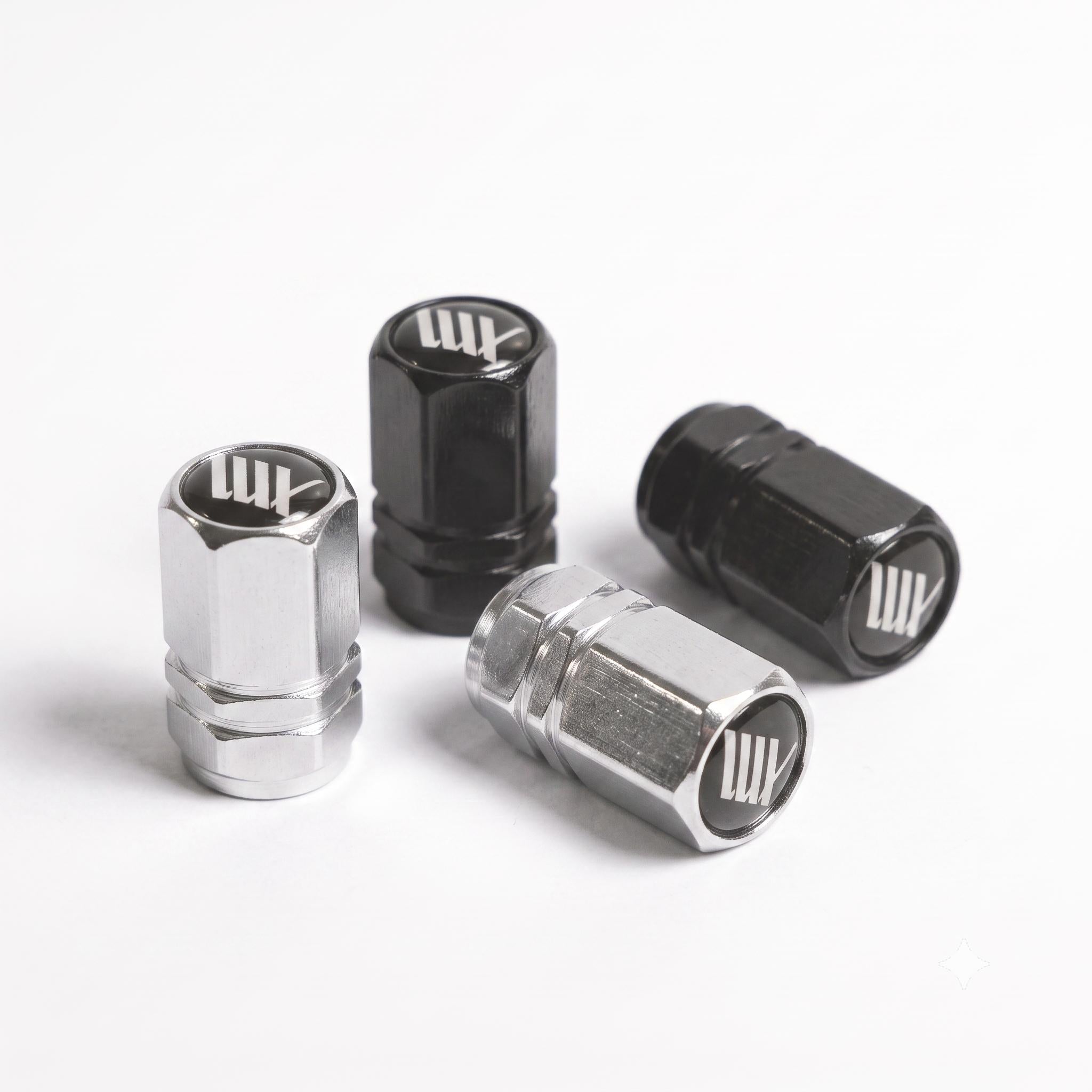 Two silver and two black LUXBMX Hex Logo Alloy Valve Caps are displayed on a white surface. Each cap features a stylized white "LW" logo on top, making these pairs standout bike accessories.