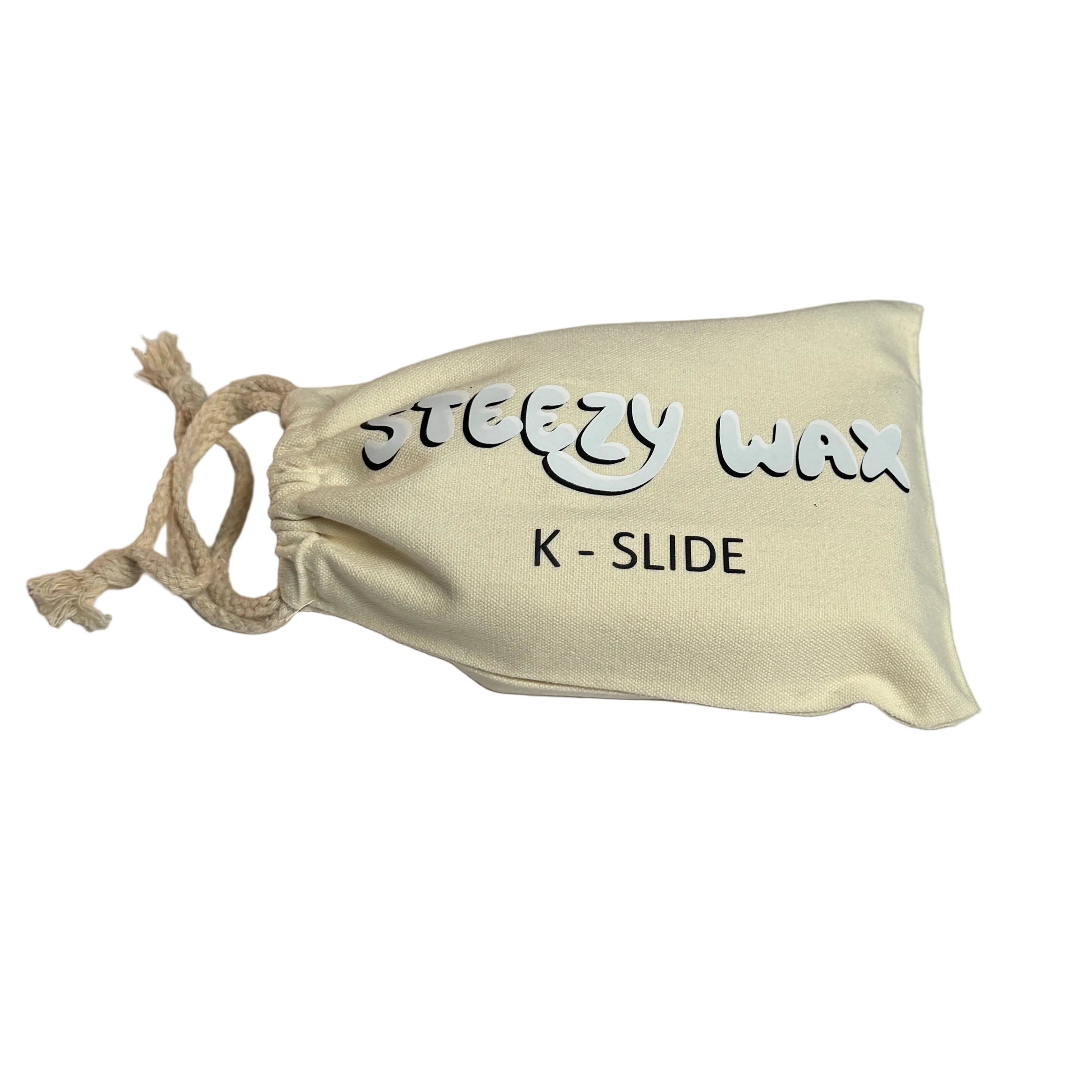 A cream-colored drawstring pouch labeled "Steezy Wax / K-Slide" rests on a plain white surface, containing premium handmade skate wax from Australia.