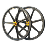 Two Skyway 24 Inch Graphite Flanged Wheels, featuring a sleek black alloy design with yellow hubs and seven spokes each, expertly crafted from carbon-fiber composite, are positioned overlapping one another.