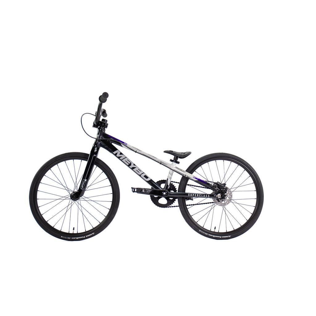 The Meybo 2026 Superclass Junior Bike is shown in black and white with a sleek frame, 22” top tube, flat handlebars, and thin tires, presented in a side view on a white background.