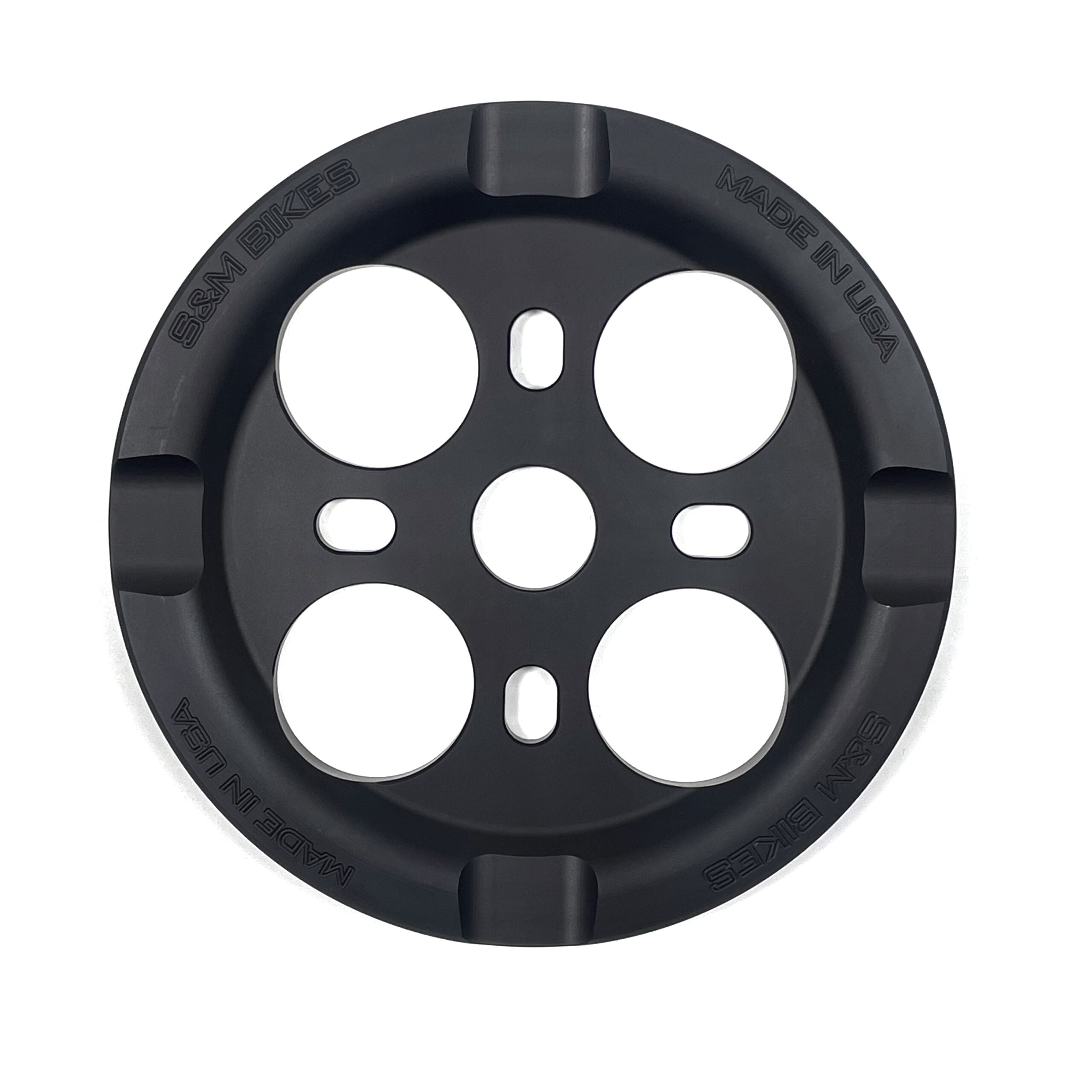 The S&M Mid School Guard Sprocket is a black, circular sprocket with four large holes and engraved “SSM BIKES” and “MADE IN USA” text around the edge, shown from above on a white background. A durable bashguard sprocket for your bike.