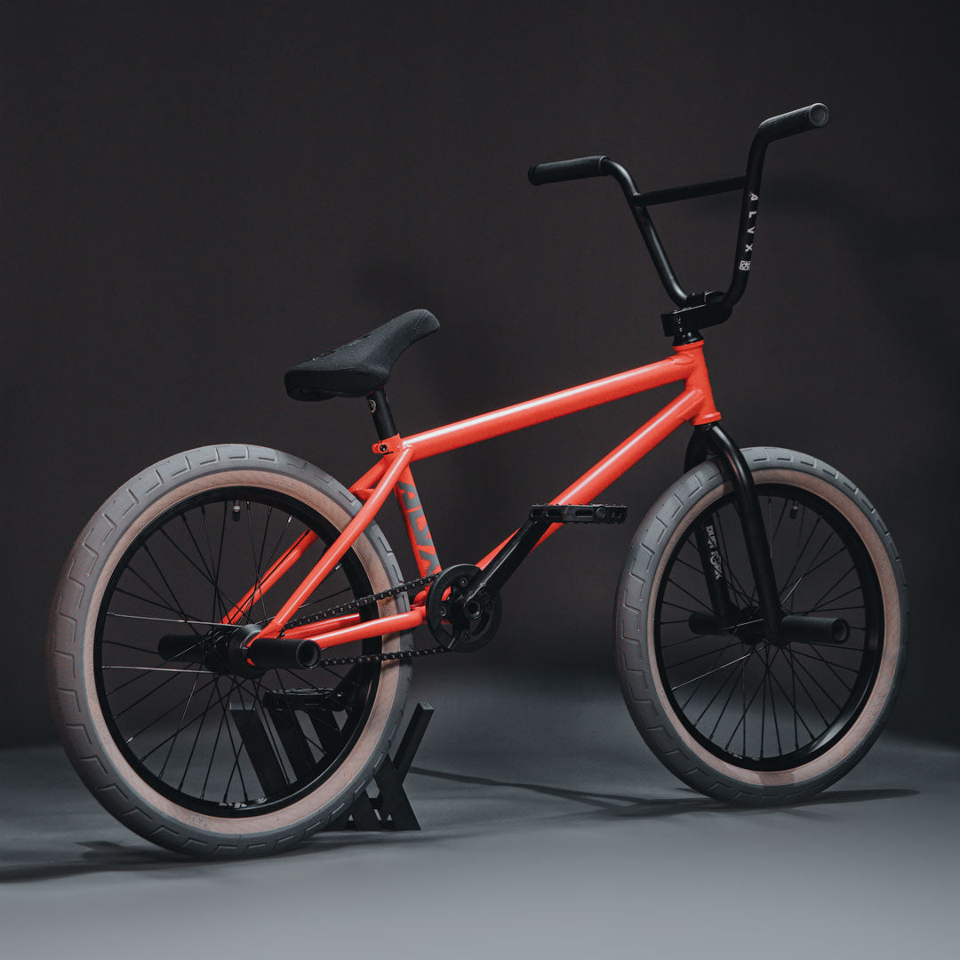 The BSD ALVX AF+ Custom 20 Inch Bike, a sleek orange bmx bike featuring aftermarket parts, is showcased against a striking black background.