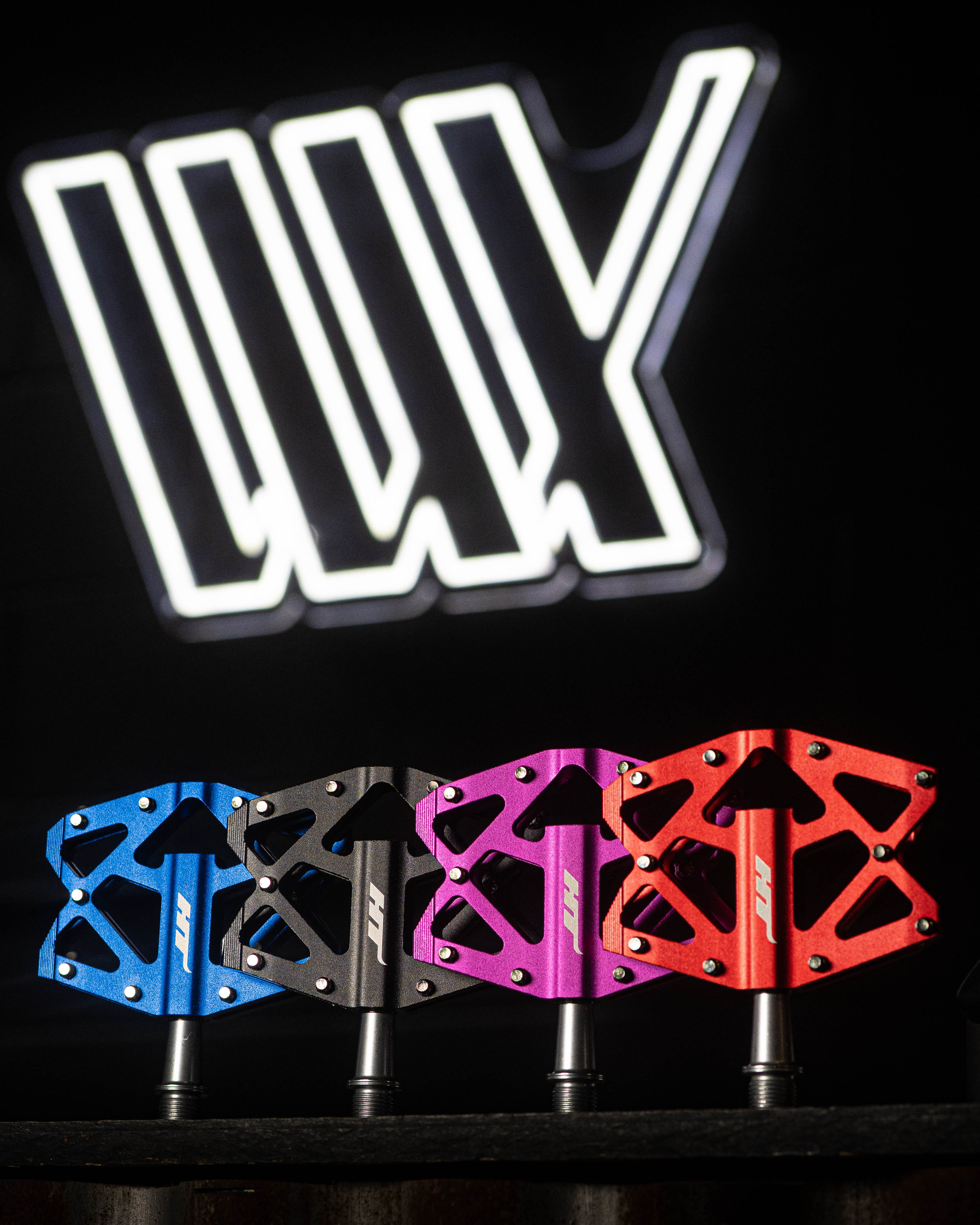 The HT AXO1A Nano Pedals in blue, black, pink, and red stand out against a dark backdrop with a white logo. Designed for lightweight performance, these pedals provide exceptional grip for cycling enthusiasts.