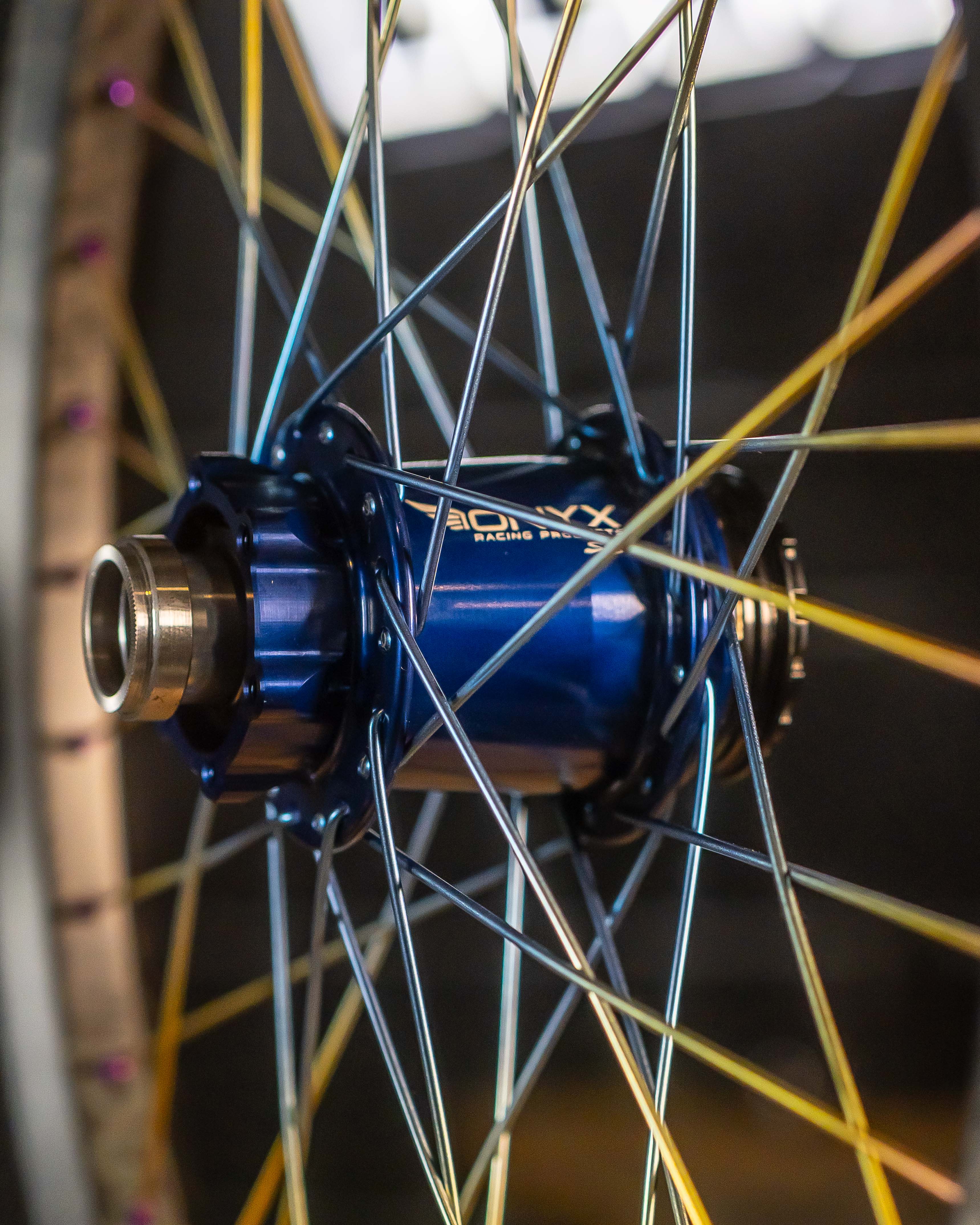 Close-up of Onyx X Spectre Carbon Marble Sunset 20 Inch Wheelset, highlighting titanium spokes and metallic components against a blurred background.