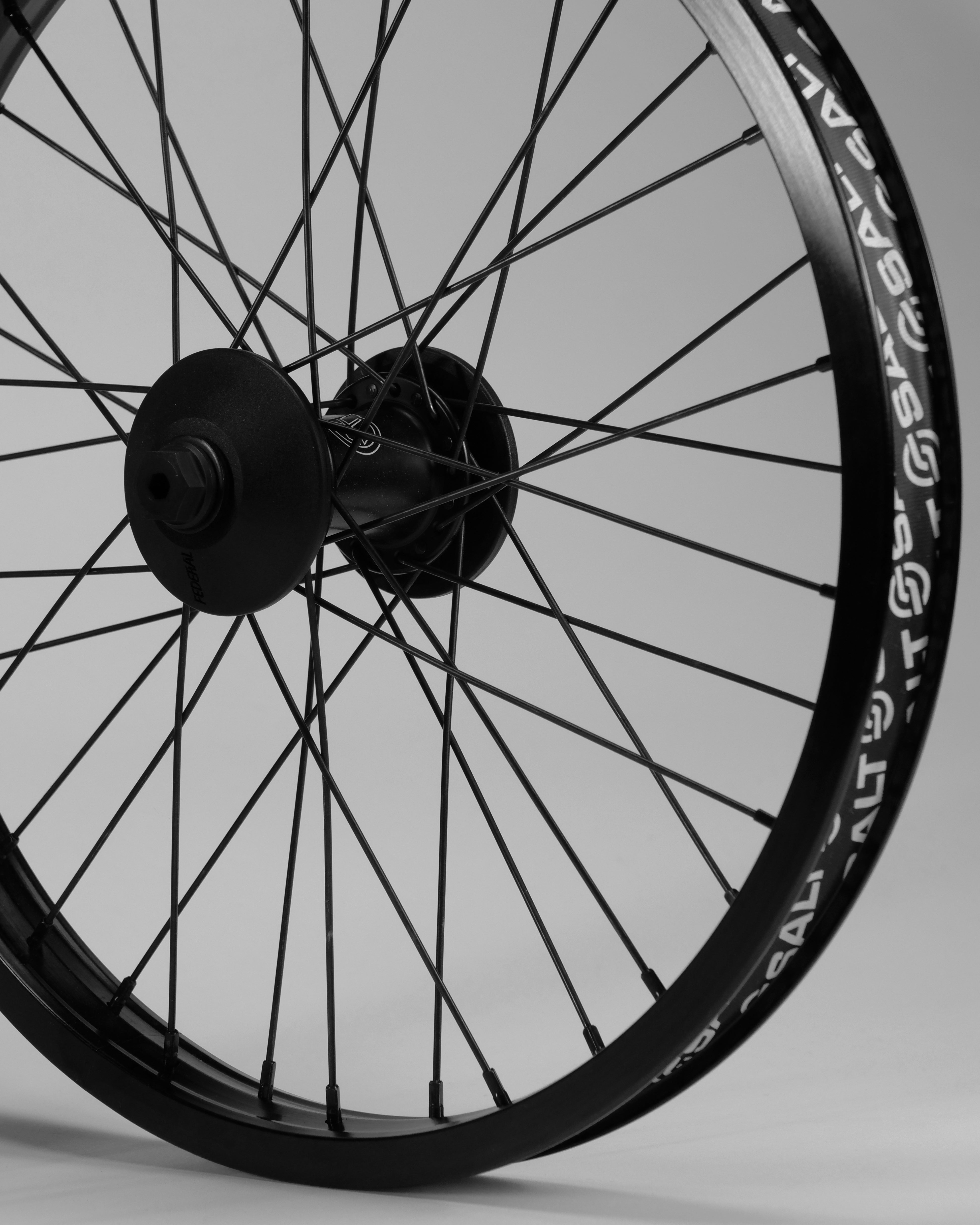 Close-up of a bicycle wheel with spokes, showing detailed view of the Federal Stance Pro x Alienation 18 Custom Wheelset hubset and rim against a neutral background.