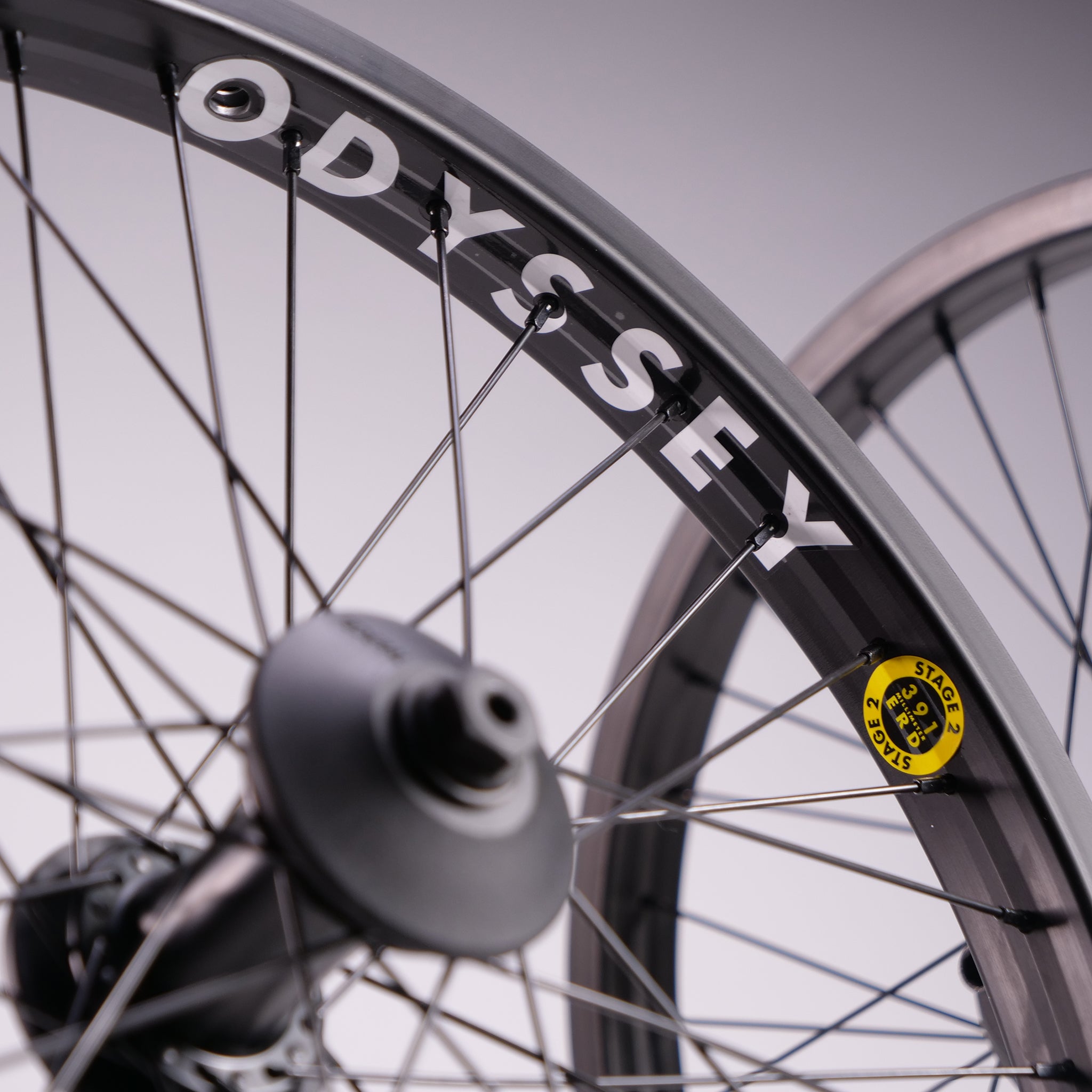 Close-up of a bicycle wheel with the word "Odyssey" on the rim and a yellow sticker labeled "Stage 3 Dual Side," featuring elements of Federal Motion x Odyssey Stage 2 Custom Wheelset.