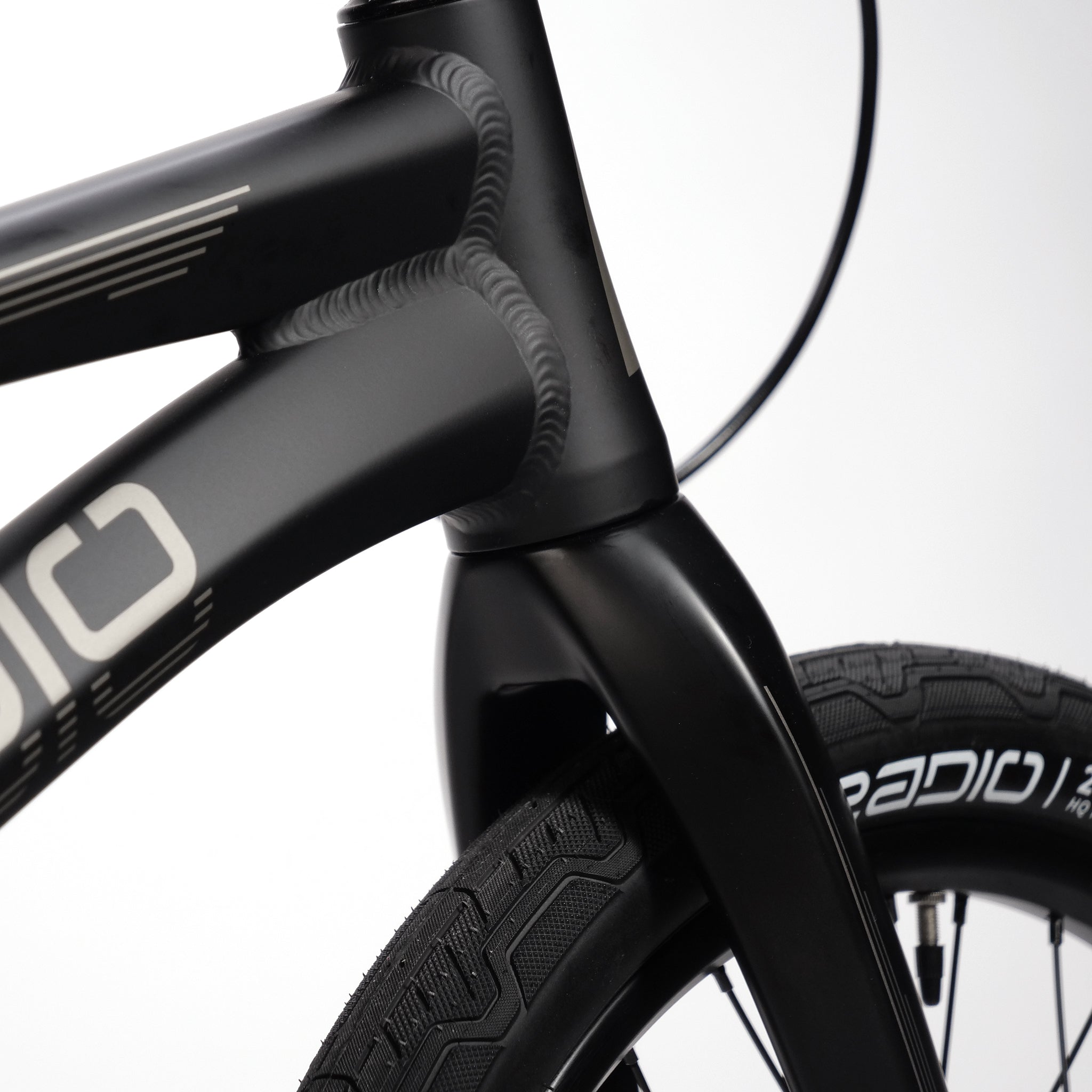 Close-up of the front end of the Radio Raceline Quartz Pro L Bike 2025, showcasing its black, hydro-formed frame along with the fork and front tire. The sidewall of the tire features the text "RADIO.