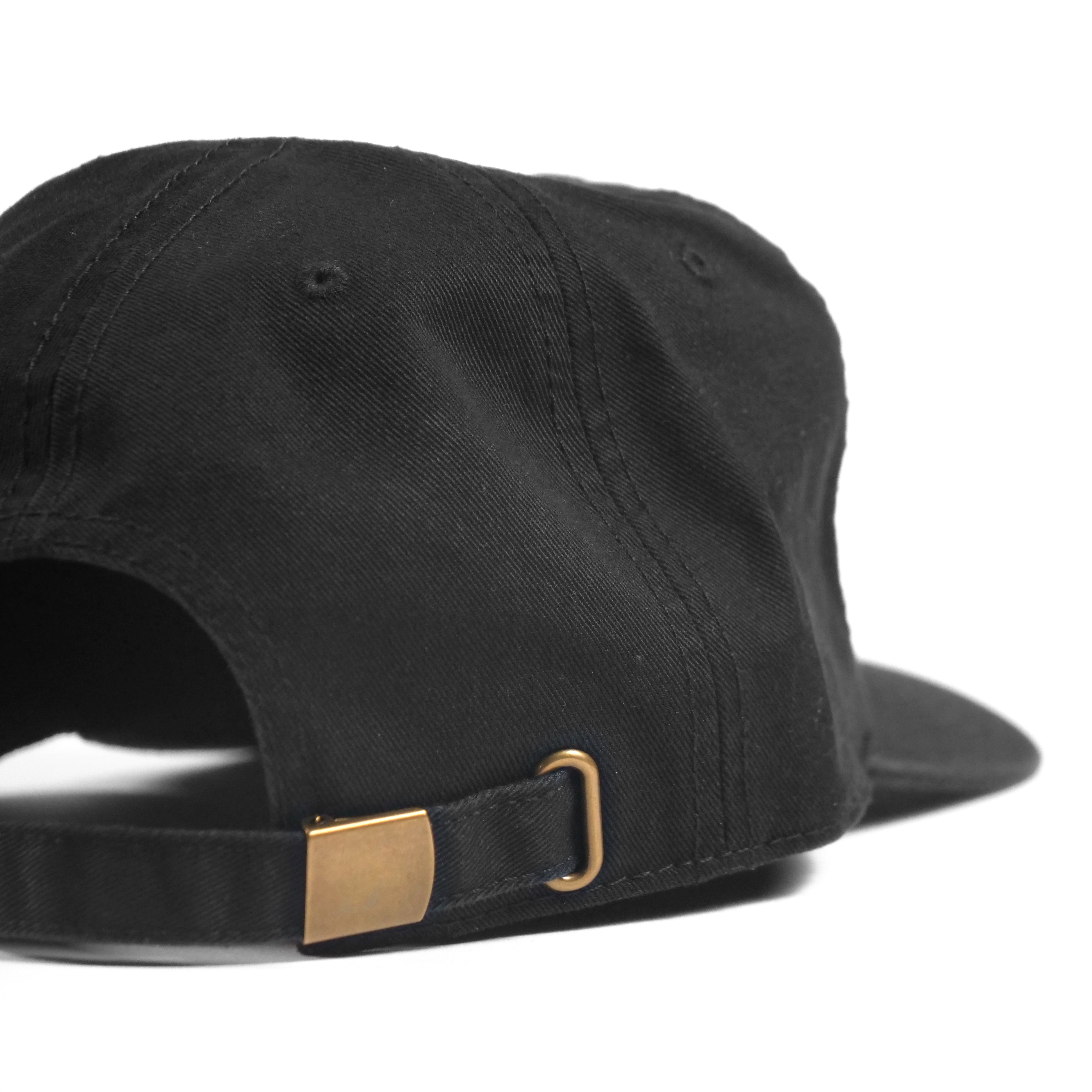 A close-up of the back of the Cactus BMX Mag Dead Cap Black, featuring an adjustable strap with a gold-colored metal buckle.
