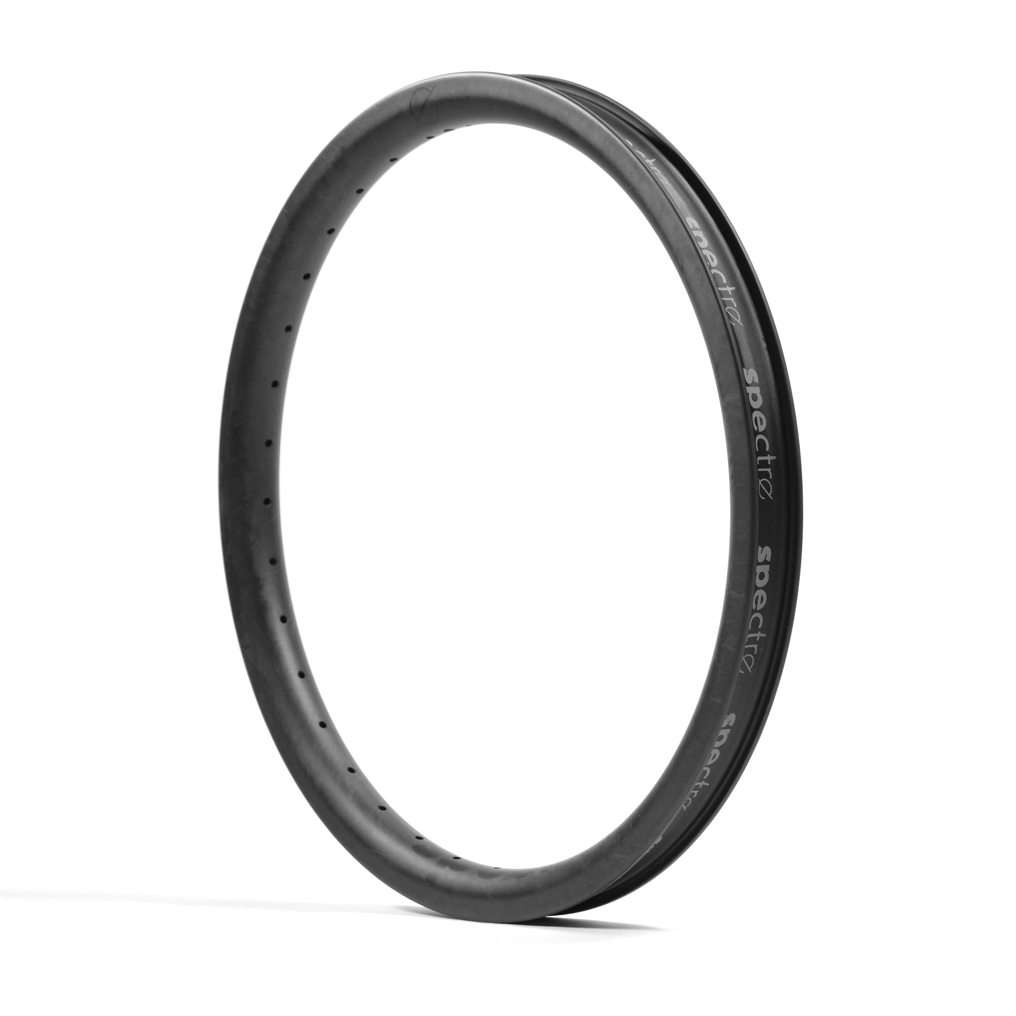 A black, round Spectre V3 Carbon Fiber 20 Inch 36H Brakeless Rim made from Toray T800 with small, evenly spaced 4D drilled holes is shown standing upright against a white background.