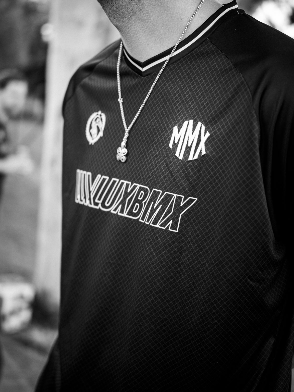 A person wearing the LUXBMX MMX Soccer Jersey—featuring a dark, stylish design with “MMX” displayed on the chest—and a clover necklace, photographed in black and white.