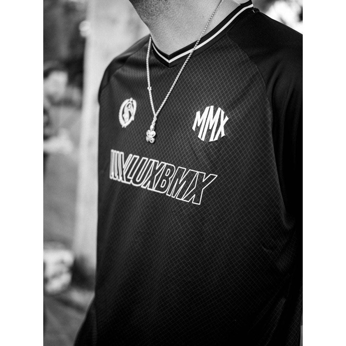 A person wearing the LUXBMX MMX Soccer Jersey—featuring a dark, stylish design with “MMX” displayed on the chest—and a clover necklace, photographed in black and white.