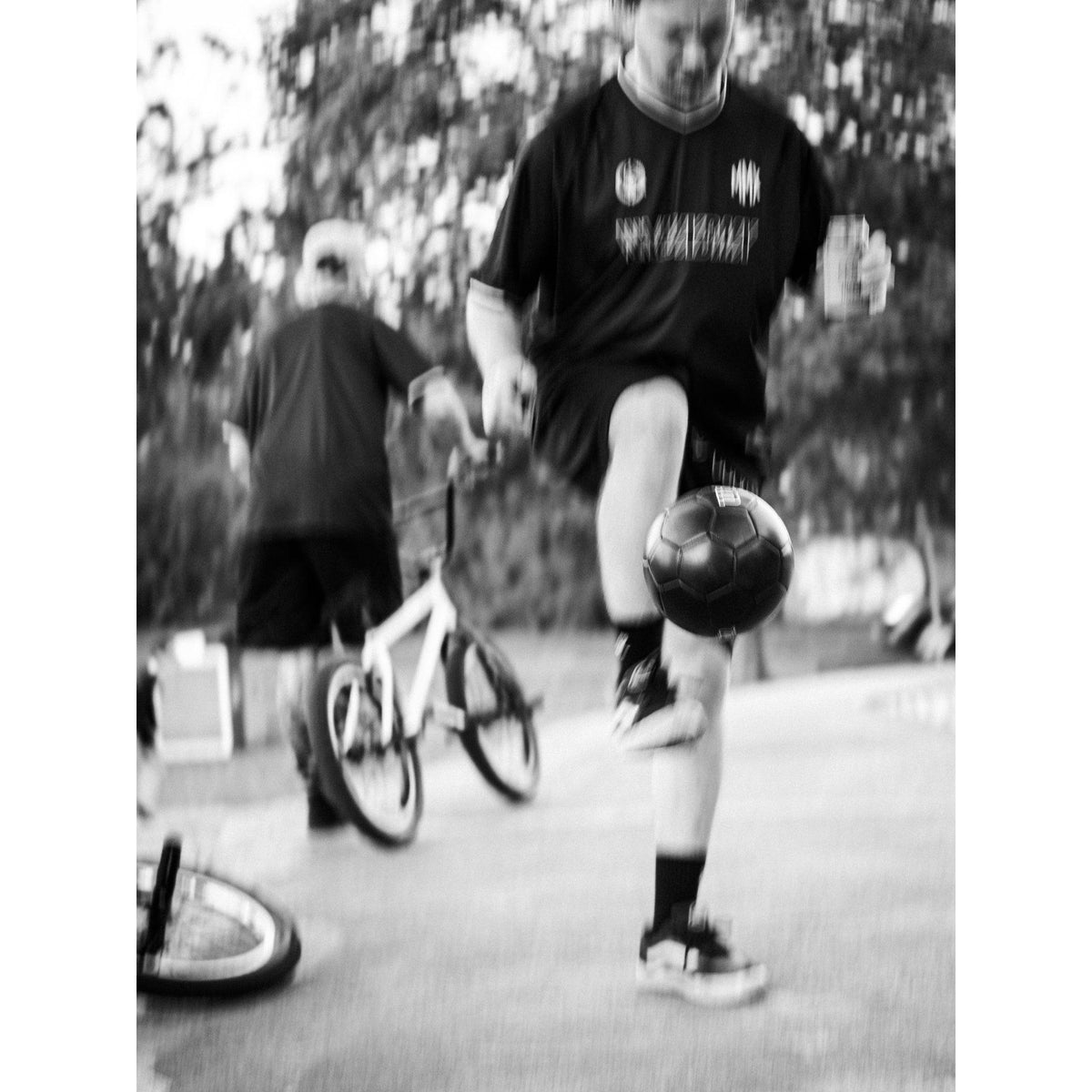 A person in sportswear juggles a soccer ball on one foot while another person stands nearby with a bicycle, wearing a breathable LUXBMX MMX Soccer Jersey - Plain Back Print.
