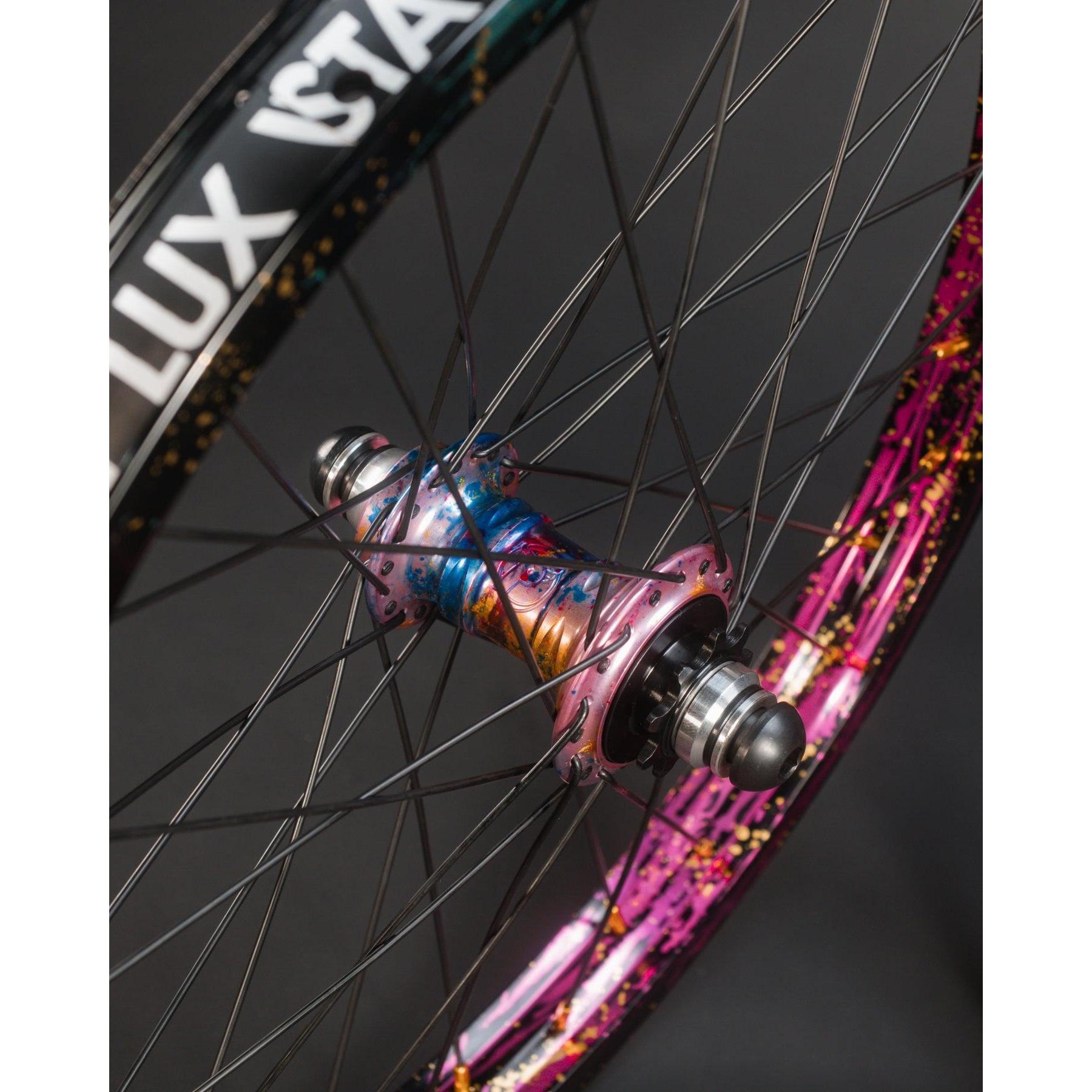 Close-up of the Profile x Odyssey Near Earth Objects Wheel Set (Limited Edition) featuring black spokes, rims with "LUX" text, and a vibrant splatter paint design.