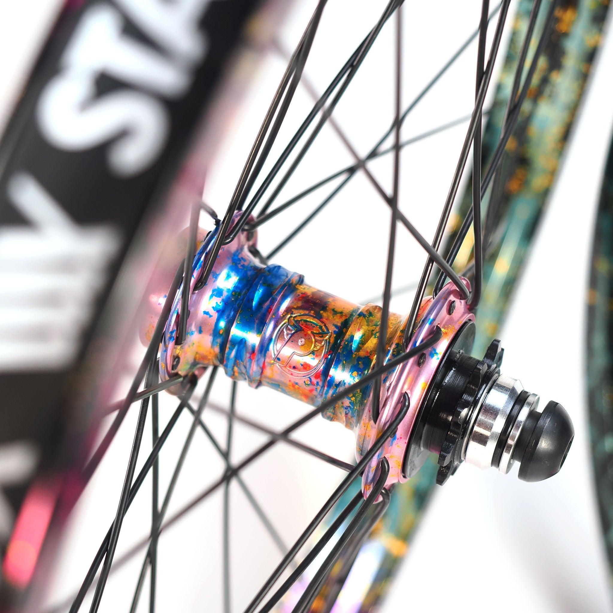 Close-up of the limited edition Profile x Odyssey Near Earth Objects Wheel Set, featuring a colorful anodized BMX hub, black spokes, and part of an Odyssey Hazard 40th Anniversary Rim in the background.