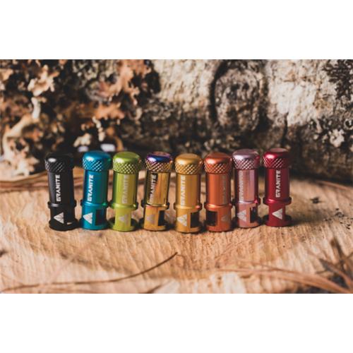 A pair of Granite Juicy CNC Presta Valve Caps with built-in valve core removers, stylish and essential bike accessories, are displayed on a wooden surface against a softly blurred natural background.