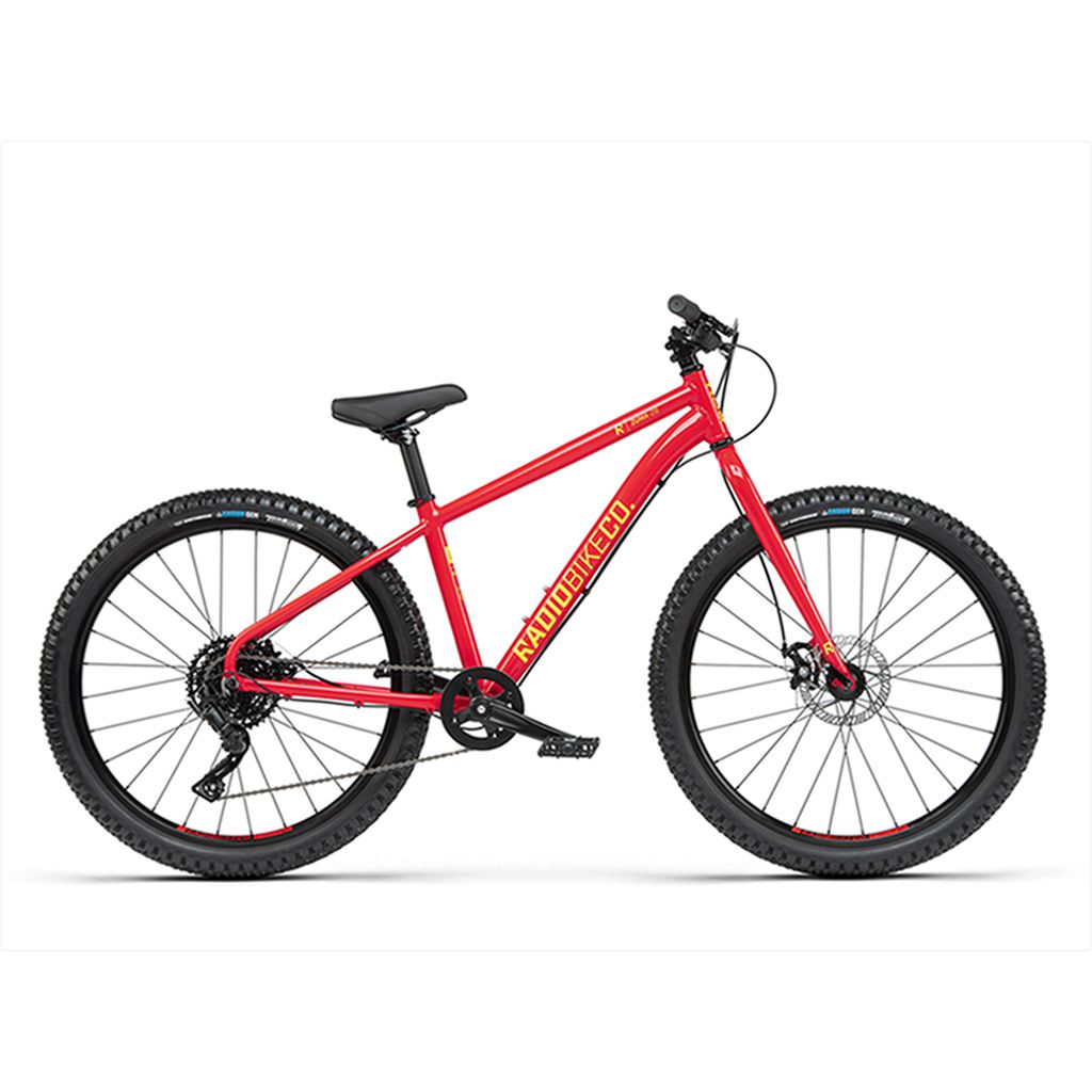 A red Radio 26 Inch Zuma Bike with thick tires, a black saddle, and the brand name "RADIO BIKES CO" displayed on its lightweight alloy frame. The kid-sized MTB is showcased on a white background.