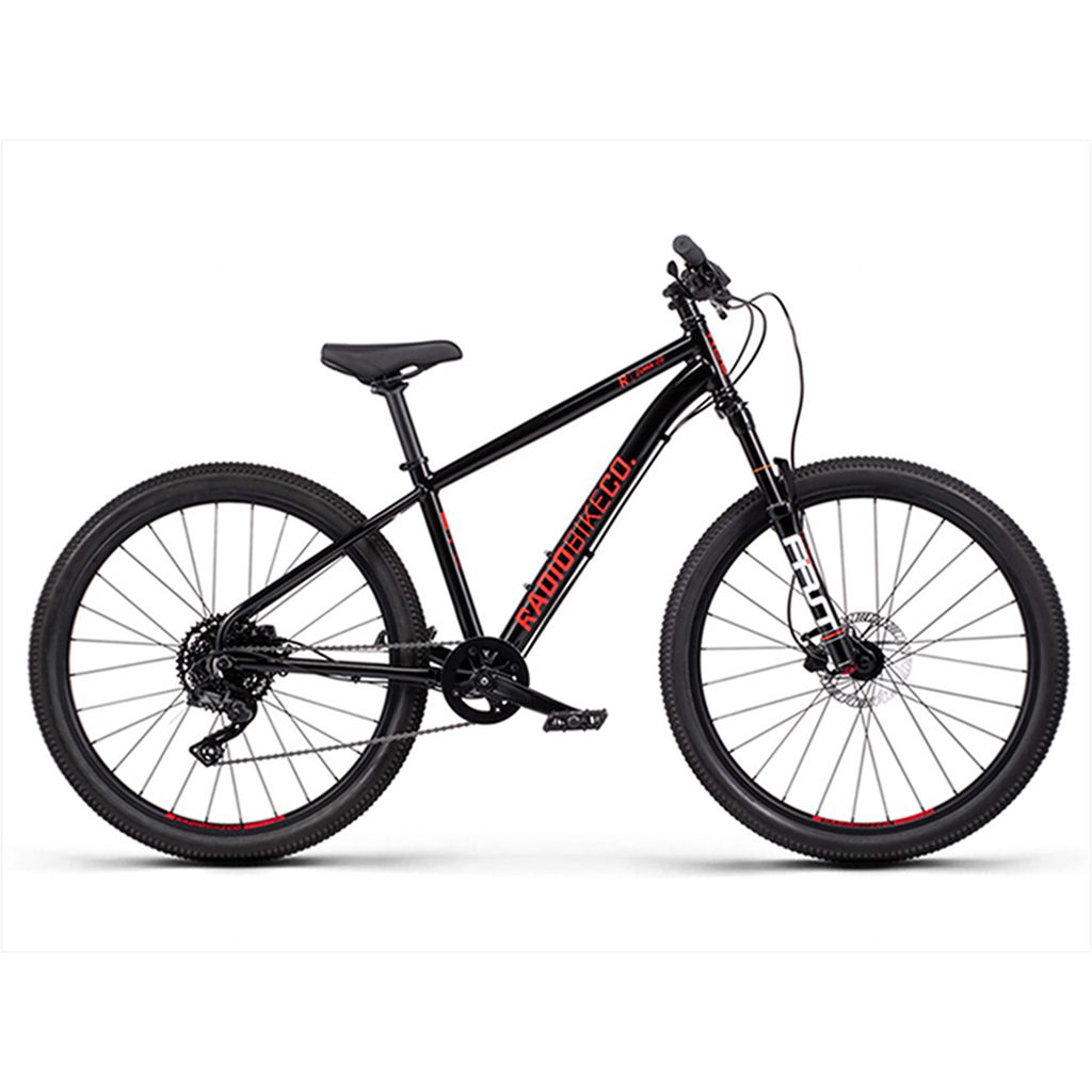 A black mountain bike with red accents, featuring thick knobby tires, a sturdy frame, and a front suspension fork. The brand name appears on the frame. This Radio 26 Inch Zuma Sus Bike is designed with children's aftermarket components for young riders seeking adventure.