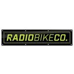 The Radio Contest Banner is a rectangular black PVC sign with yellow-green "RADIOBIKECO." text and edge mounting holes—ideal for outdoor use or displaying your favorite BMX brand.