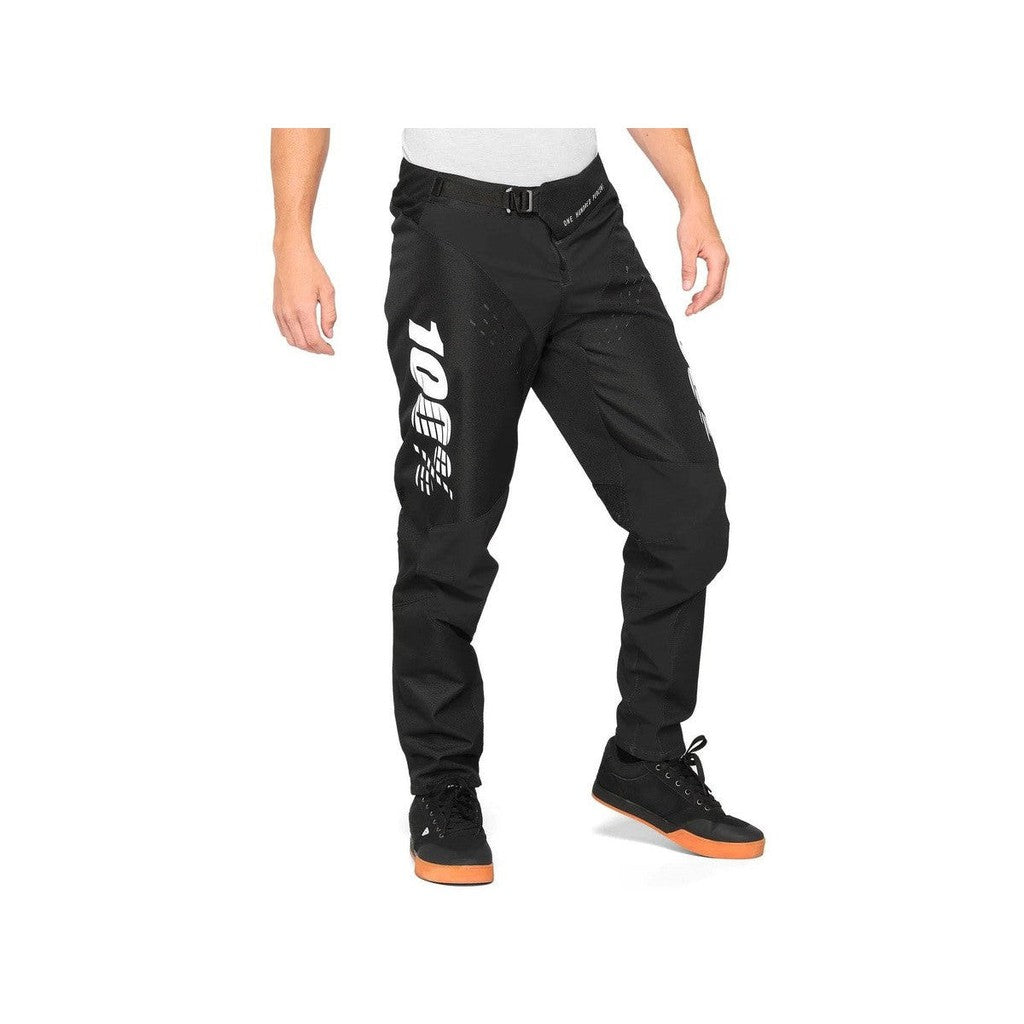 A man is wearing 100% R-Core Youth Race Pants, made with lightweight materials, while standing in front of a white background.