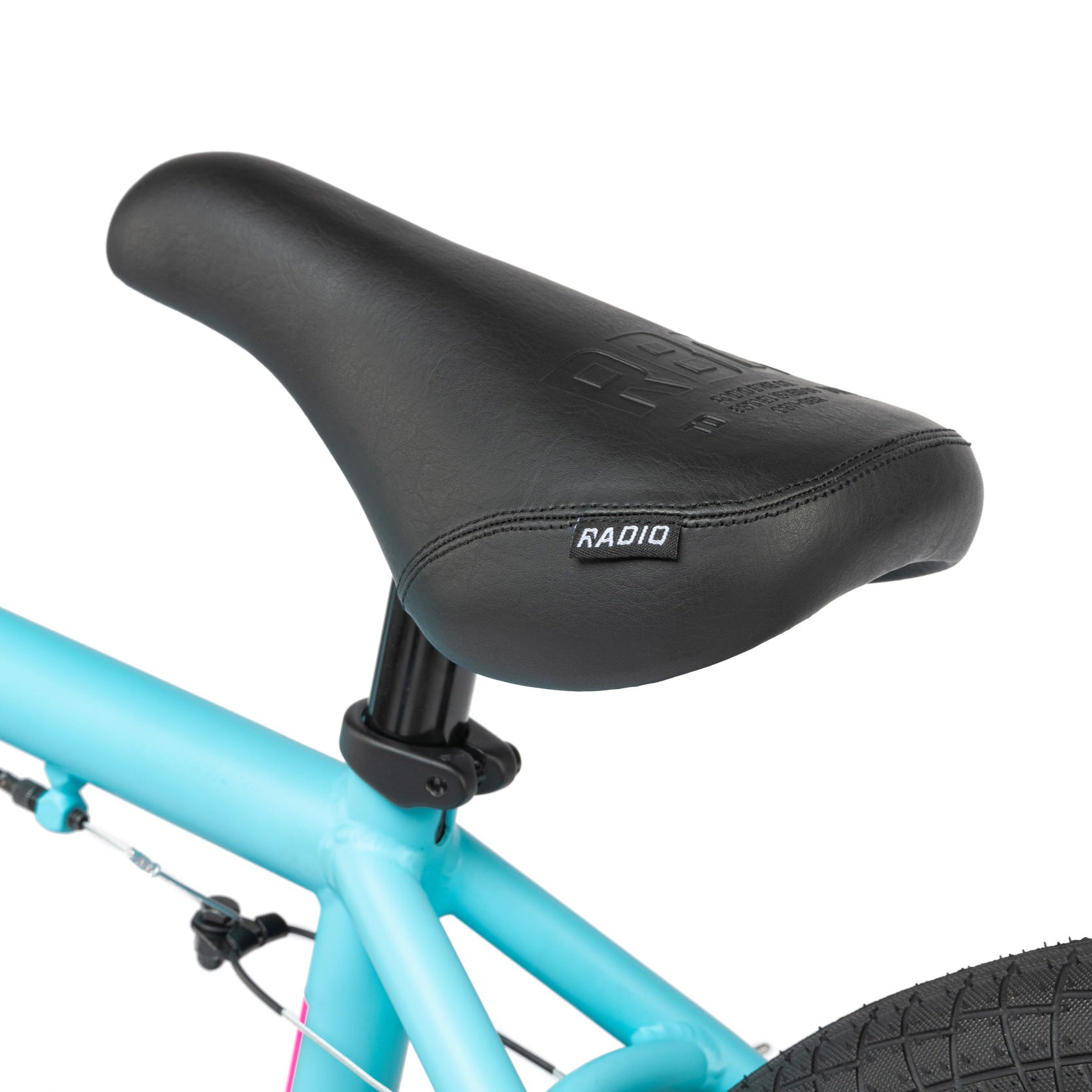 Close-up of a black bicycle saddle mounted on the light blue frame of the Radio Evol 20 Inch Bike, showcasing part of the rear tire and brake cables in the background. Perfect for beginner riders, this bike features high-quality components.