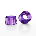Two SD-X Sniper Evo 10mm Bolt Caps, metallic purple and made from 7075 aluminum, rest on a white surface—one upright, one lying flat—with subtle reflections visible.