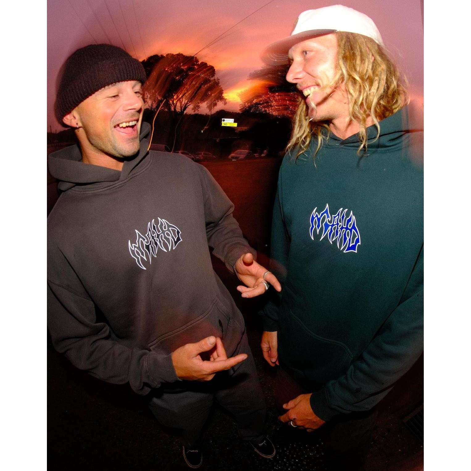 Two men in beanies and hoodies stand outside at sunset, laughing and talking. One points at the other's Mahd Metal Hoodie.