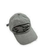 The V1da Shoreline Cap is a distressed gray strapback, crafted from 100% cotton, with a bold black embroidered abstract logo on the front.