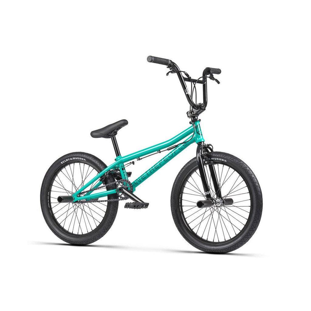 The Wethepeople Sinus Flatland 20 Inch Bike in teal features black handlebars, a black seat, and flatland-specific Mugen tires, designed for tricks and stunts. The bike is displayed from a side angle against a white background.