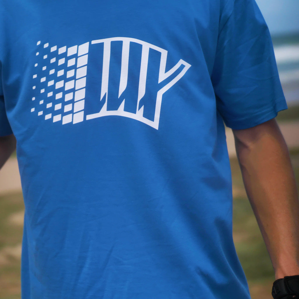 A man wearing a LUXBMX Y2K Tee - Royal Blue, made of breathable fabric, holding a surfboard.