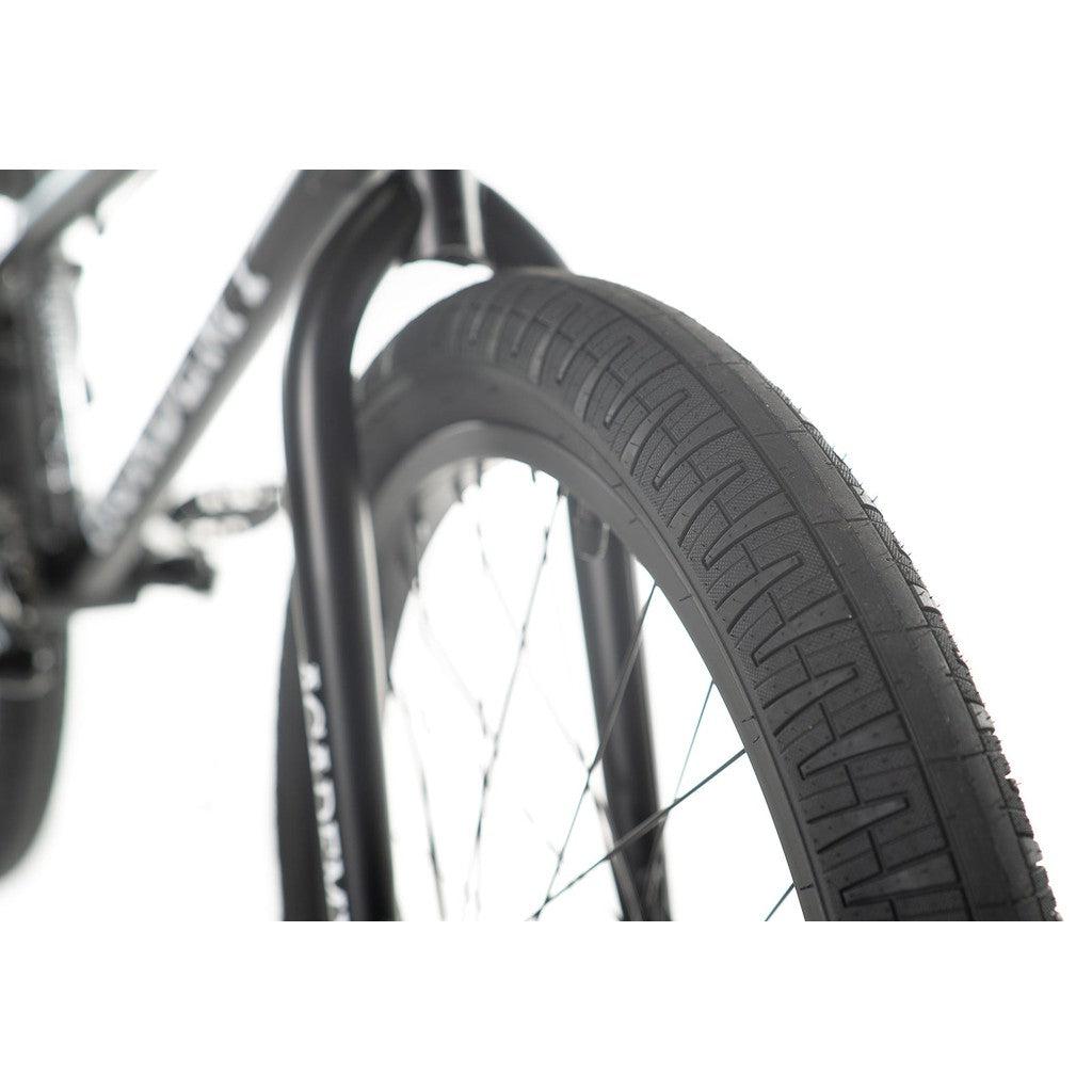 Close-up of the front tire of a bicycle with a black frame, showcasing the tire tread pattern and rim spokes, typically found on entry-level BMX bikes like the Academy Entrant 20 Inch Bike.