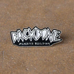 The Backbone Always Building Pin showcases graffiti-style "BACKBONE" and "ALWAYS BUILDING" text on a textured brown background. This pin symbolizes resilience, making it ideal for softgoods lovers and unique pin collectors, representing steadfast dedication.