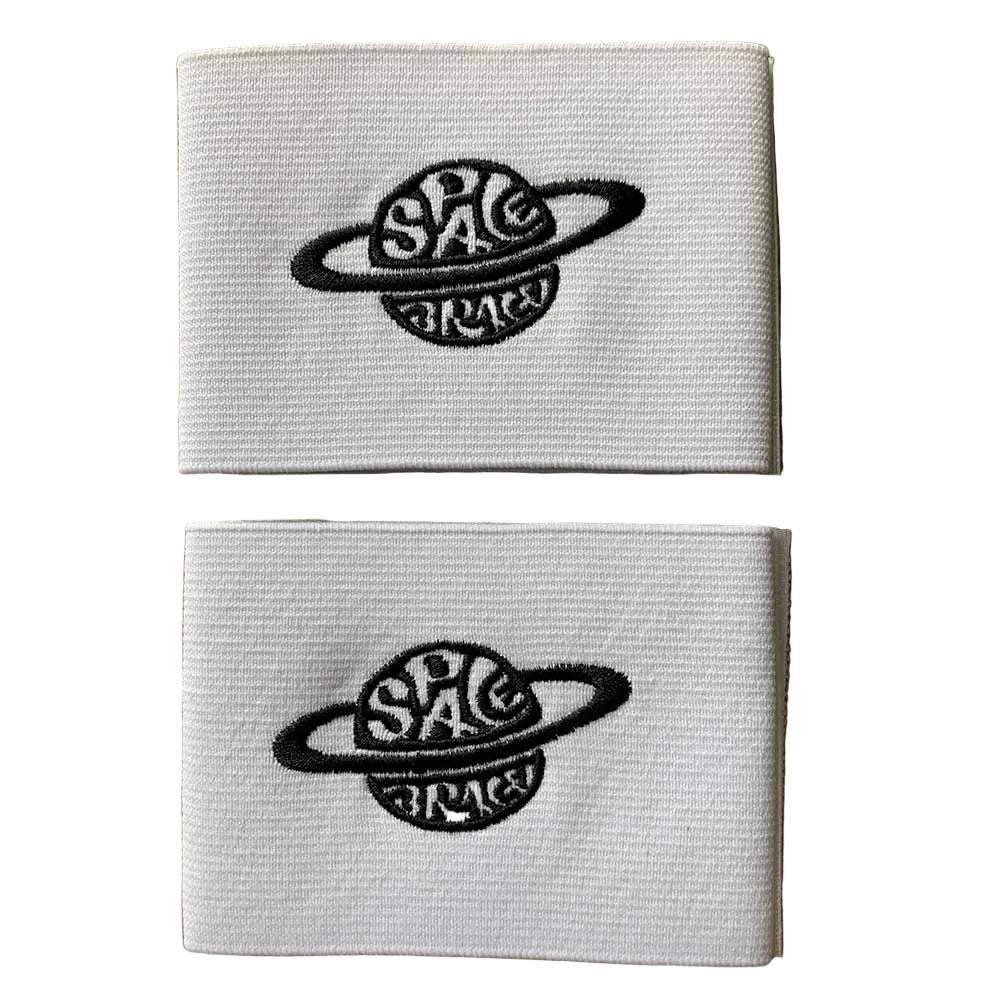Two folded white Space Brace Ankle 2.0 Cover Straps featuring a black embroidered planet and the words “SPACE” and “BRACE,” stacked on a wooden surface—designed as replacement straps for added ankle support, comfort, and style.