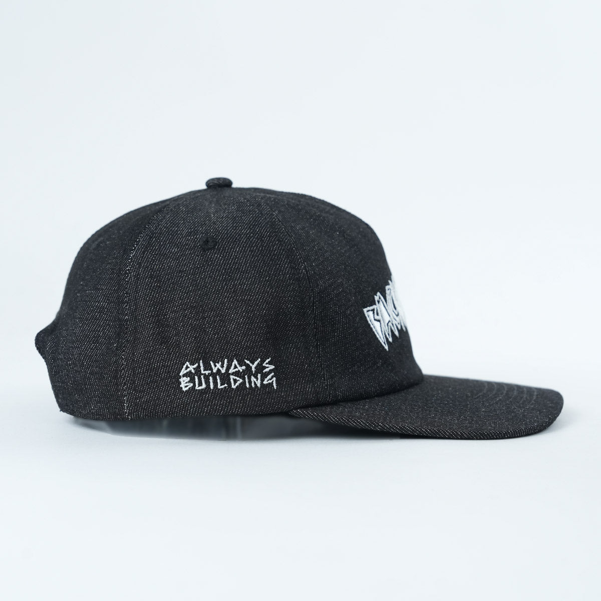 The Backbone Always Building Hat is a black unstructured 5-panel cap featuring “ALWAYS BUILDING” embroidered in white on the left side and a white graphic on the front, displayed against a plain background.