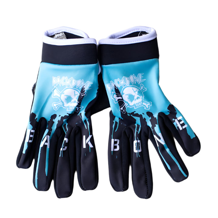 A pair of Backbone Gnar Drip Adult Gloves in blue and black, showcasing a skull and crossbones design, is laid flat on a concrete surface. Made from lightweight spandex, these gloves prominently feature the word "BACKBONE.